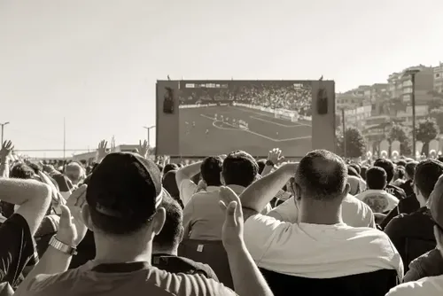 Publikum verfolgt Public Viewing auf großer Leinwand im Freien